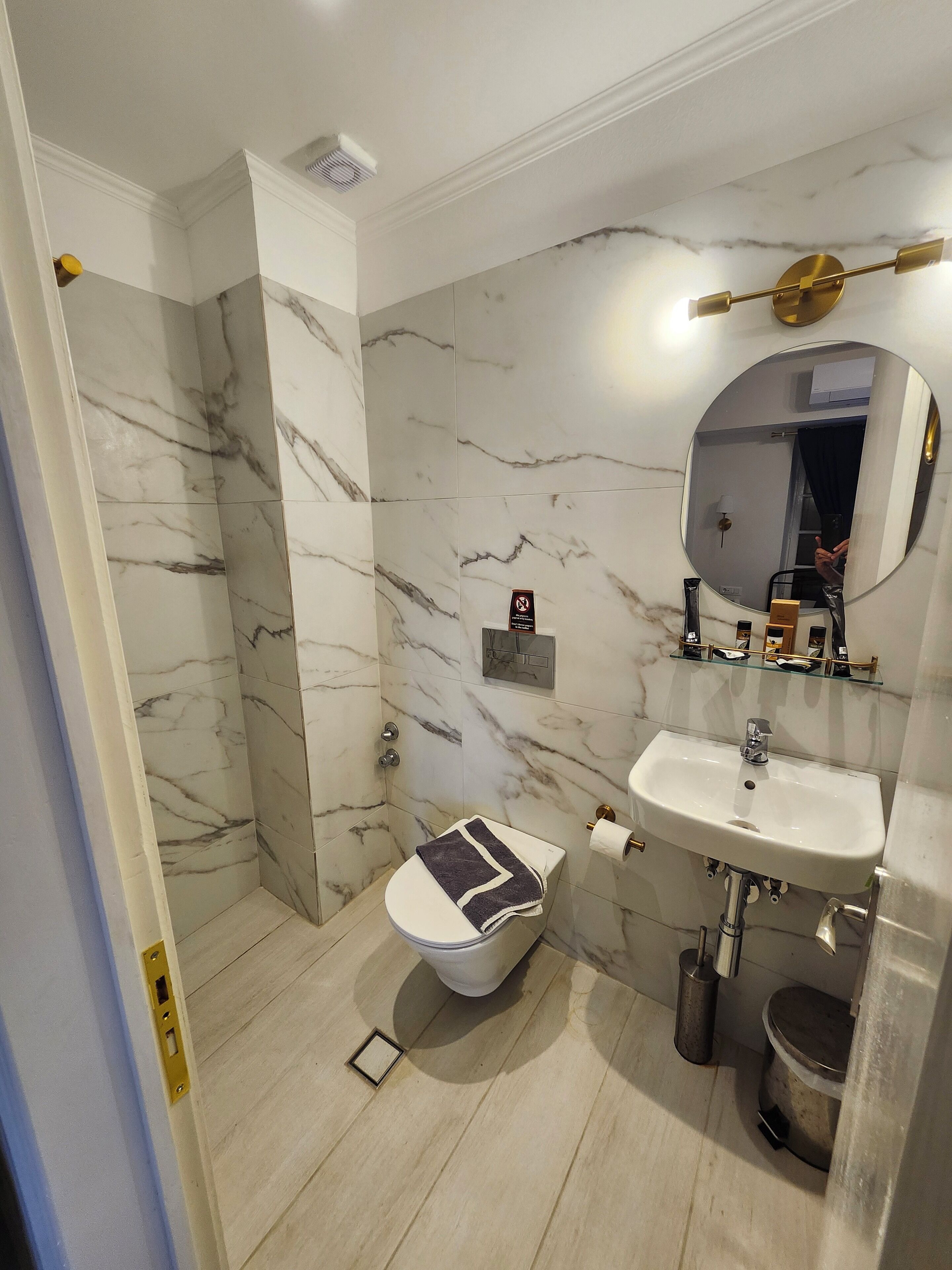 A modern bathroom with a marble wall, a white toilet, a sink, and a shower area.
