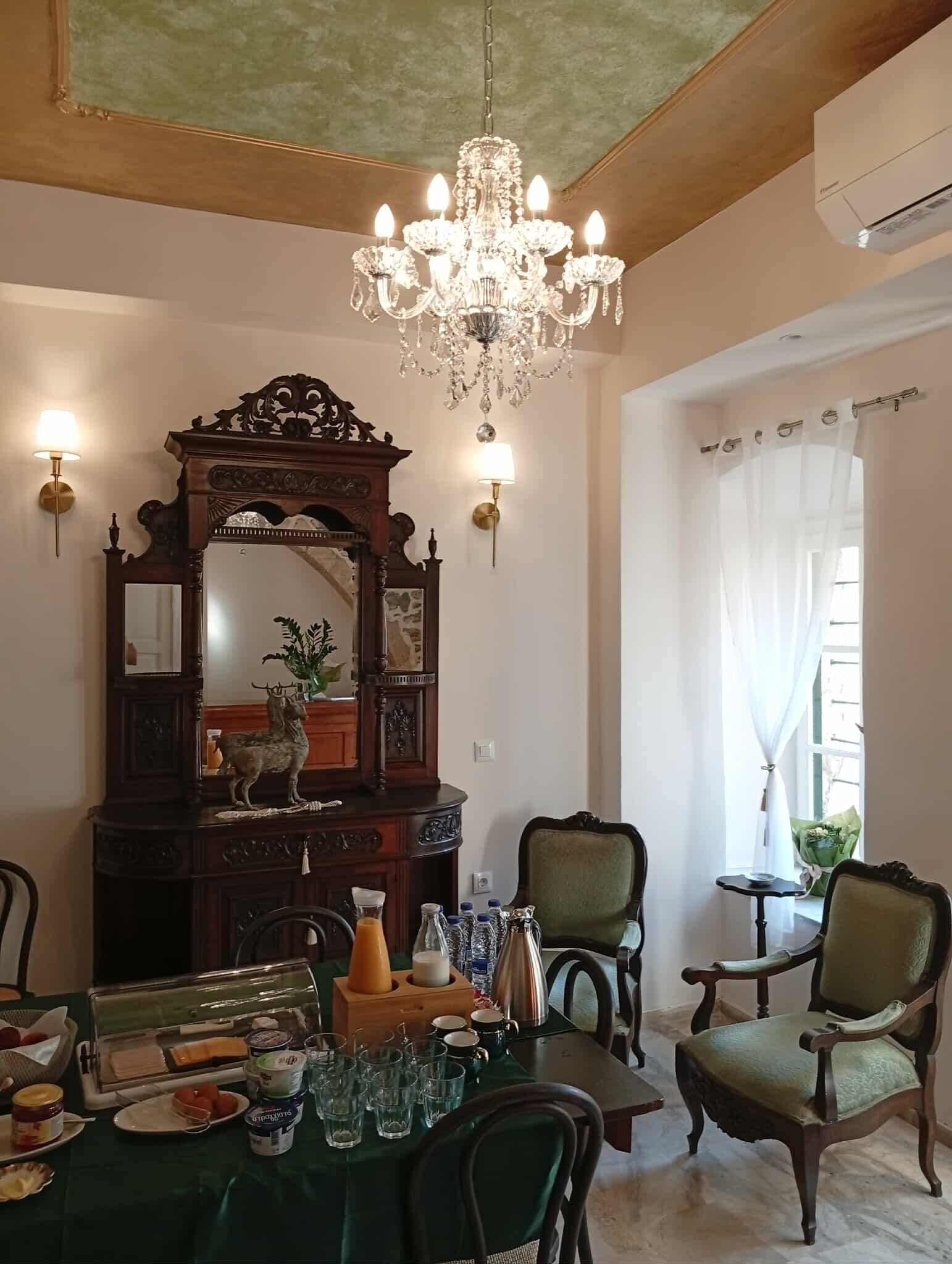 A dining area with a chandelier, ornate mirror, and a table set for breakfast.