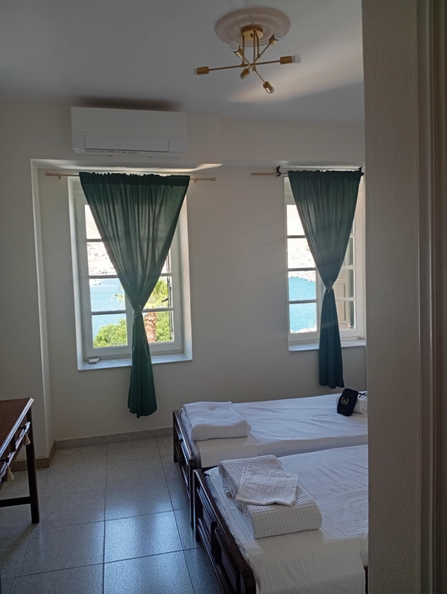 Habitación de hotel con dos camas, un ventilador de techo y vista al mar a través de las ventanas.