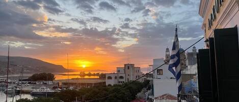 A coastal town at sunset with buildings, a flag, and a marina.