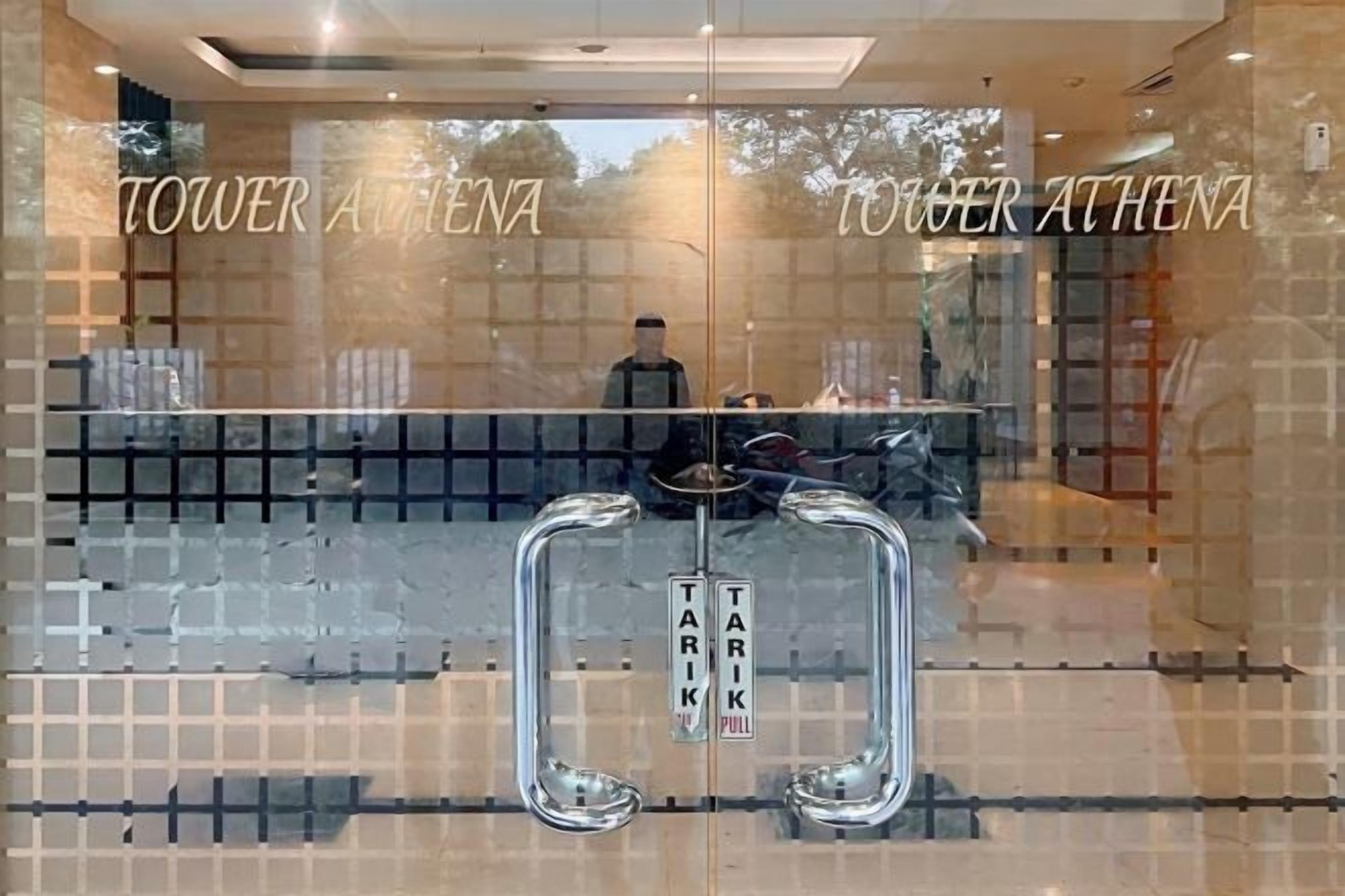 A hotel reception area with a glass partition, a reception desk, and the name 'TOWER ATHENA' on the glass.