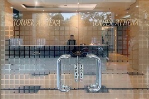Un espace d’accueil d’hôtel avec une cloison en verre, un comptoir de réception et le nom « TOWER ATHENA » inscrit sur le verre.