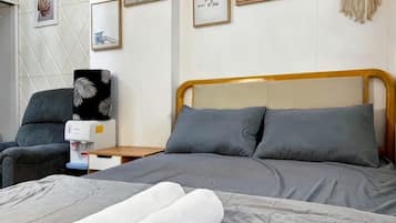 A hotel room with a bed, a chair, a nightstand, and a wall with framed pictures.