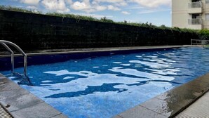 A swimming pool with a metal ladder, surrounded by a stone wall and a building with balconies.