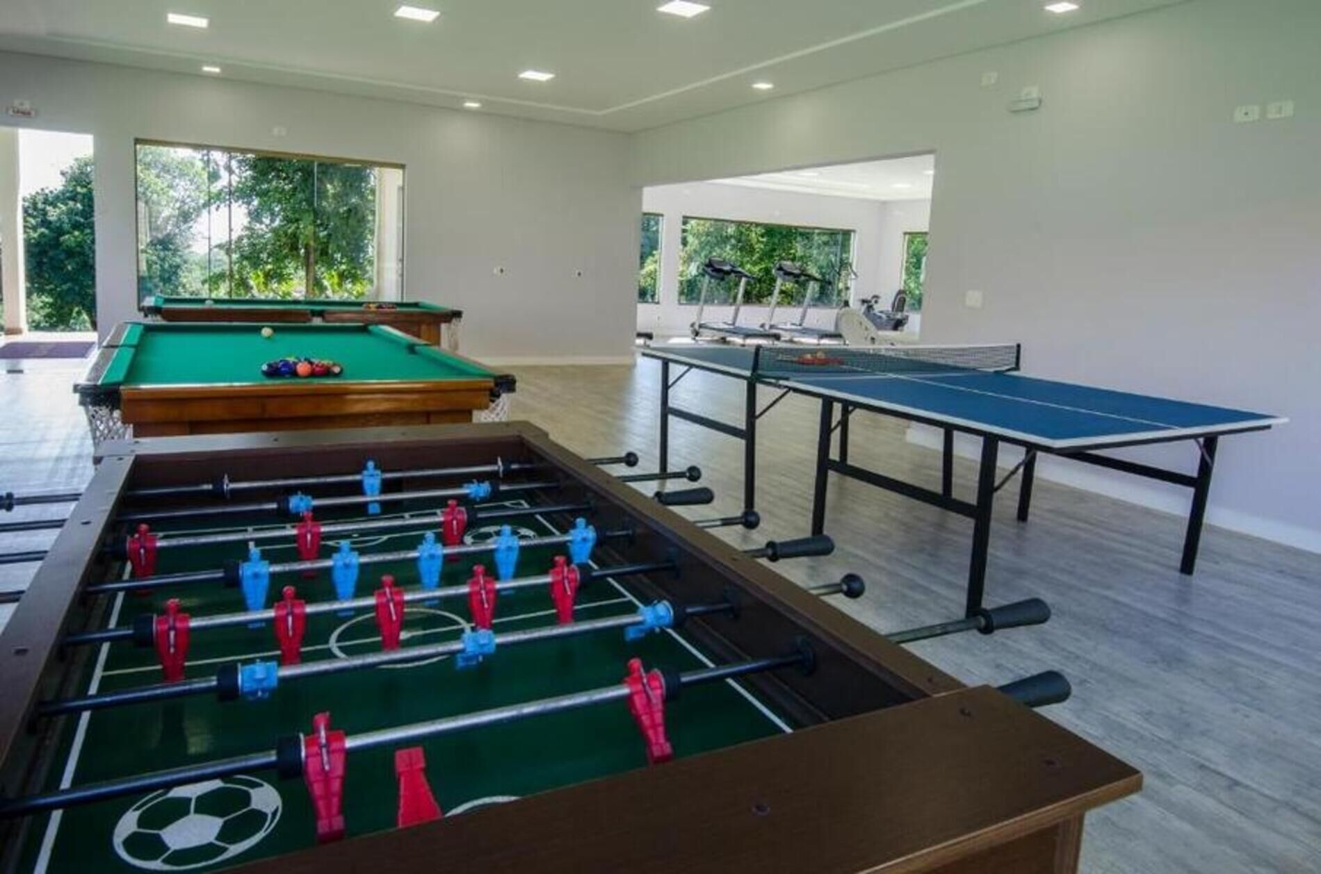 A room with a foosball table, a pool table, and a ping pong table.