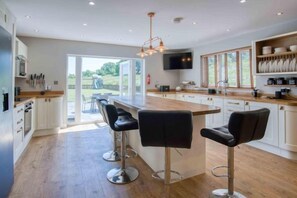 A modern kitchen with a central island, bar stools, and a television. - Hopkins Retreat Farm - 5 Bedroom House - Swansea (Mawr)