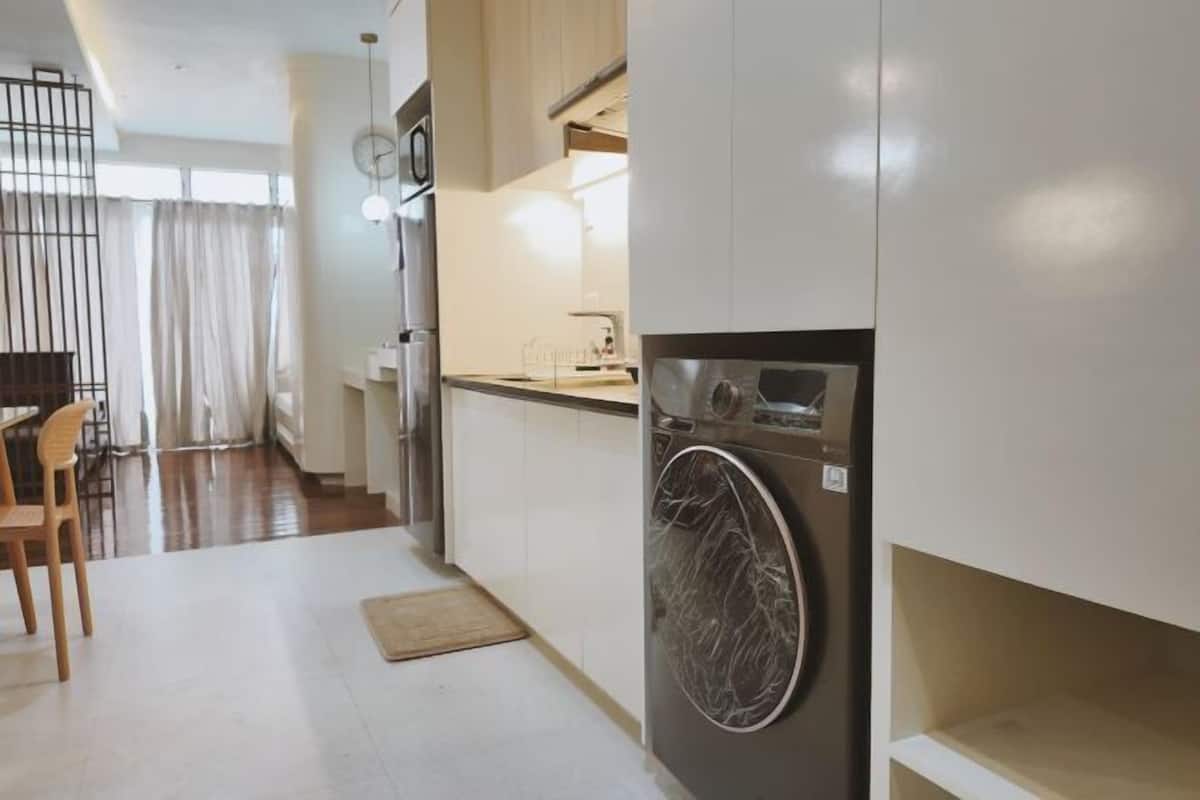 Une cuisine moderne équipée d’un lave-linge et d’un sèche-linge intégrés, un coin repas avec une chaise, et une vue sur le salon.