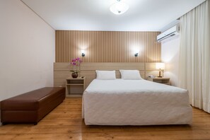 A hotel room with a large bed, two bedside tables, a nightstand, a bench, and an air conditioning unit. - Refined Premium Suite | Free Breakfast, Pool Bar & 5 mi to Bird Park (Paraná)