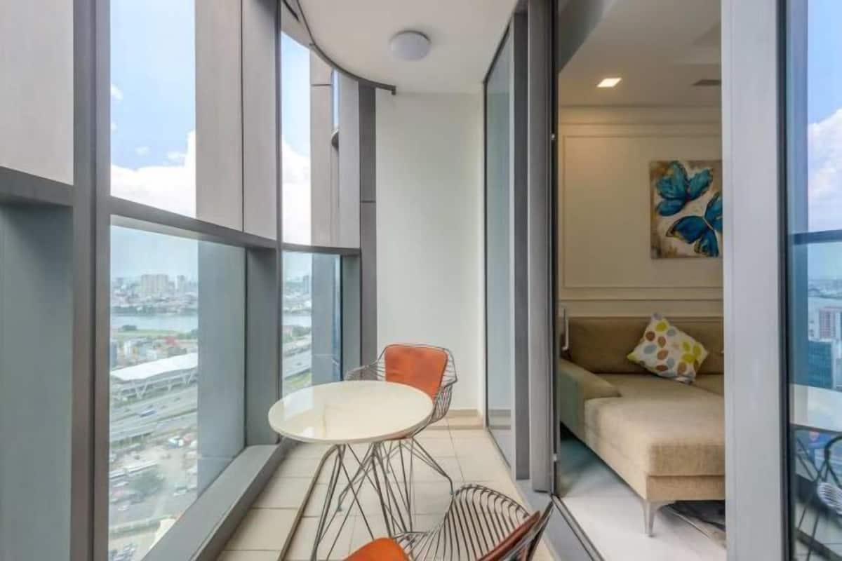 A high-rise apartment with a balcony, a dining table, two chairs, a sofa, and a city view.