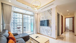A modern living room with a sofa, a coffee table, and a TV. There is a balcony with a view of buildings. - Landmark Center Saigon (Ho Chi Minh City)