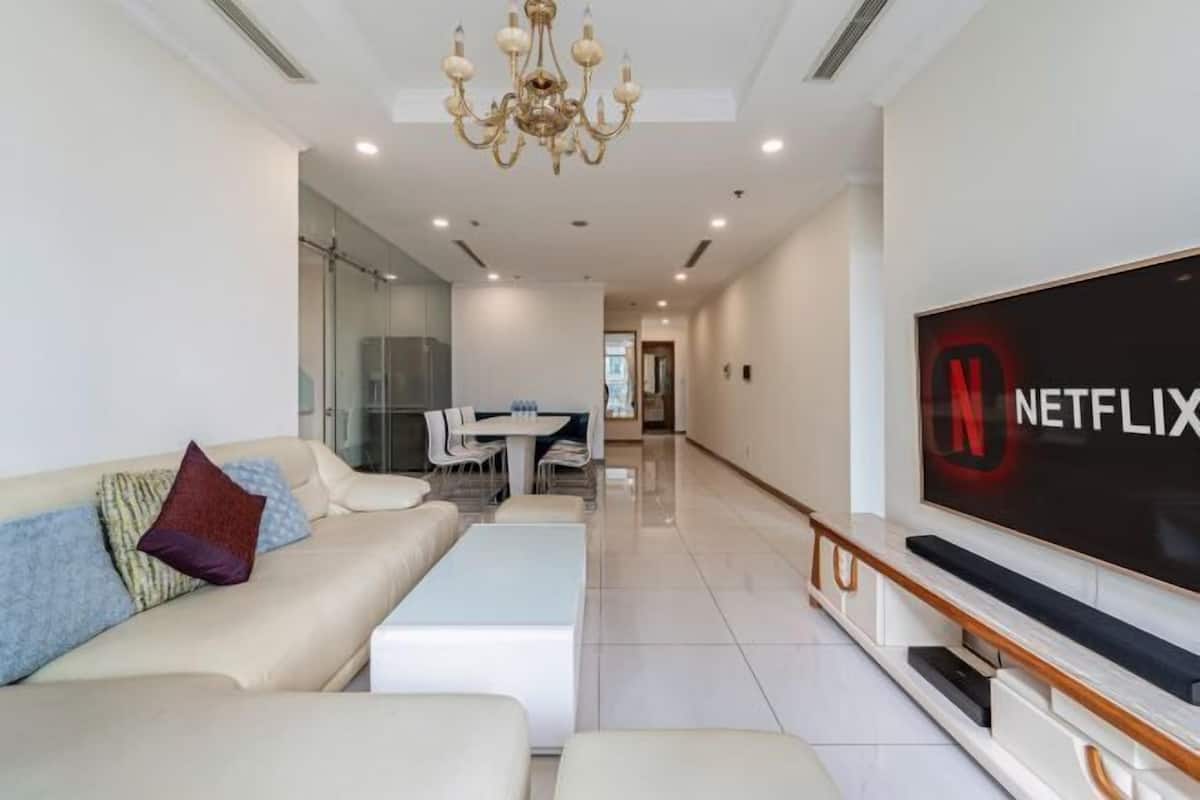 A modern living room with a sofa, a coffee table, a TV with a Netflix logo, and a dining area in the background.