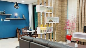 Ein modernes Wohnzimmer mit blauer Akzentwand, einem Ecksofa, einer Essecke mit Tisch und Stühlen sowie einem dekorativen Regalsystem.