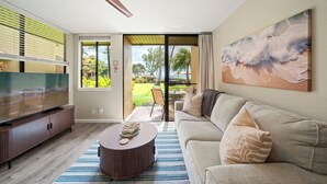 Una sala moderna con un televisor de pantalla plana, un sofá, una mesa de centro y un ventanal que ofrece vistas a un jardín y una zona de estar al aire libre.