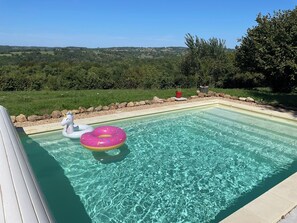 Une piscine aux eaux cristallines, agrémentée de deux bouées gonflables, entourée d’un jardin aménagé et offrant une vue sur des collines lointaines.