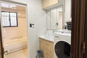 A compact bathroom with a bathtub, a washing machine, and a mirror above the sink. - Casa Alegria (Osaka)