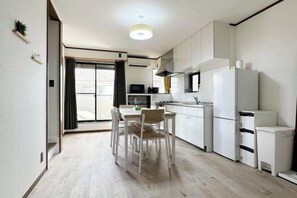 A modern kitchen with white cabinets, a dining table with chairs, and a refrigerator. - Casa Alegria (Osaka)