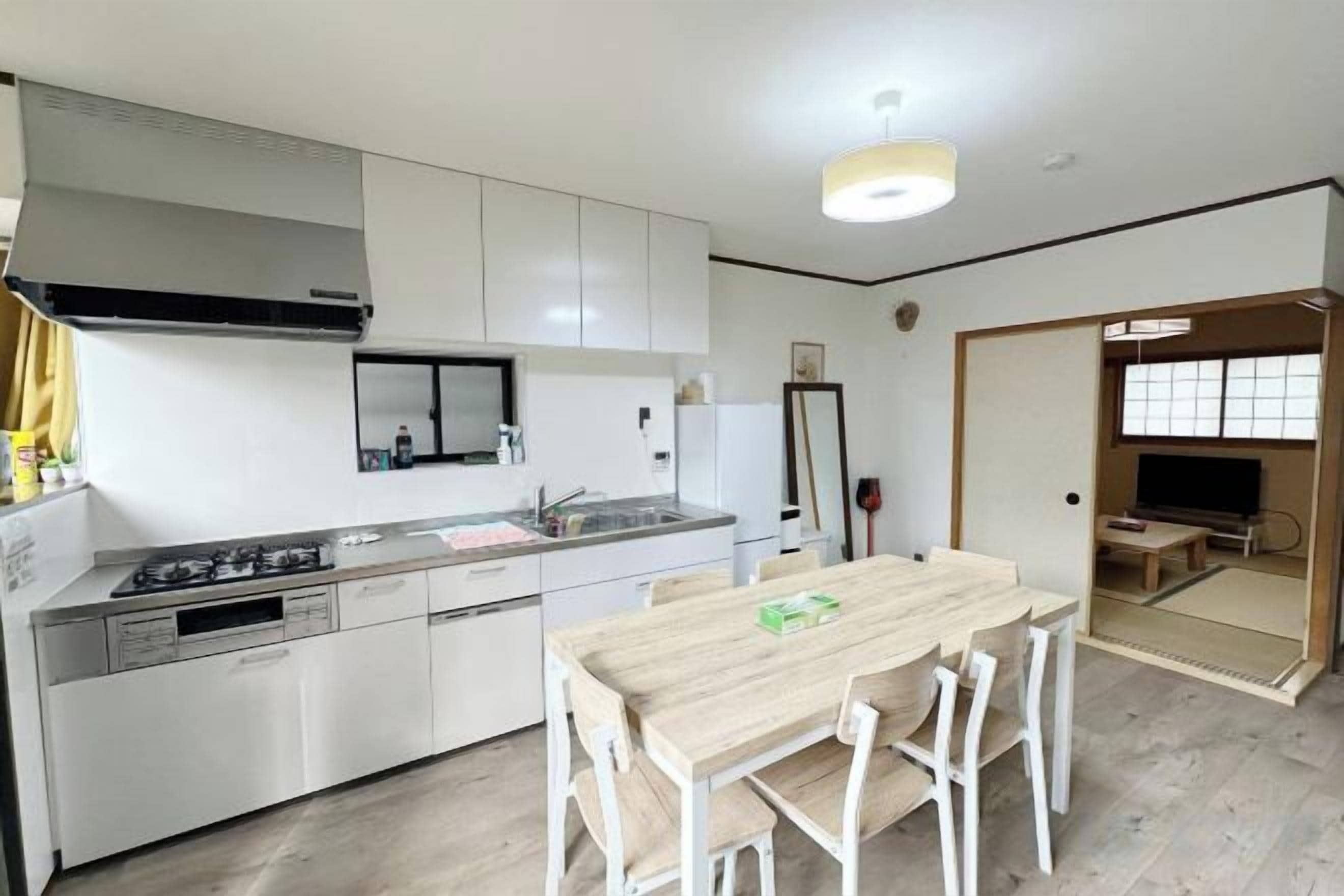 A modern kitchen with white cabinetry, a dining table with chairs, and a large window.