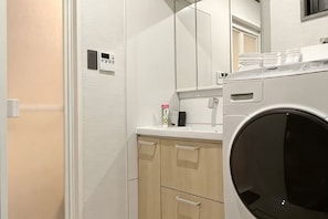 A compact bathroom with a washing machine, a mirror, and a small countertop. - Casa Alegria (Osaka)