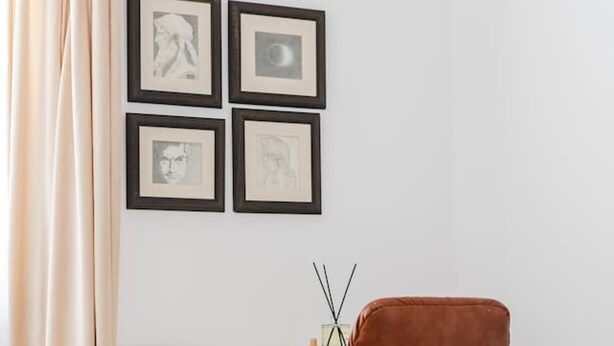 Una habitación con una única silla marrón, una mesa con marco negro y cuatro cuadros en la pared.