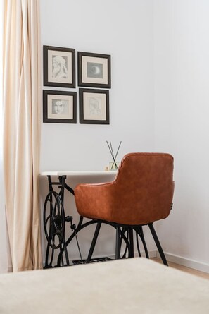 A room with a single brown chair, a table with a black frame, and four framed pictures on the wall. - Sophie Downtown Apartment Modern 1BR (Tirana)