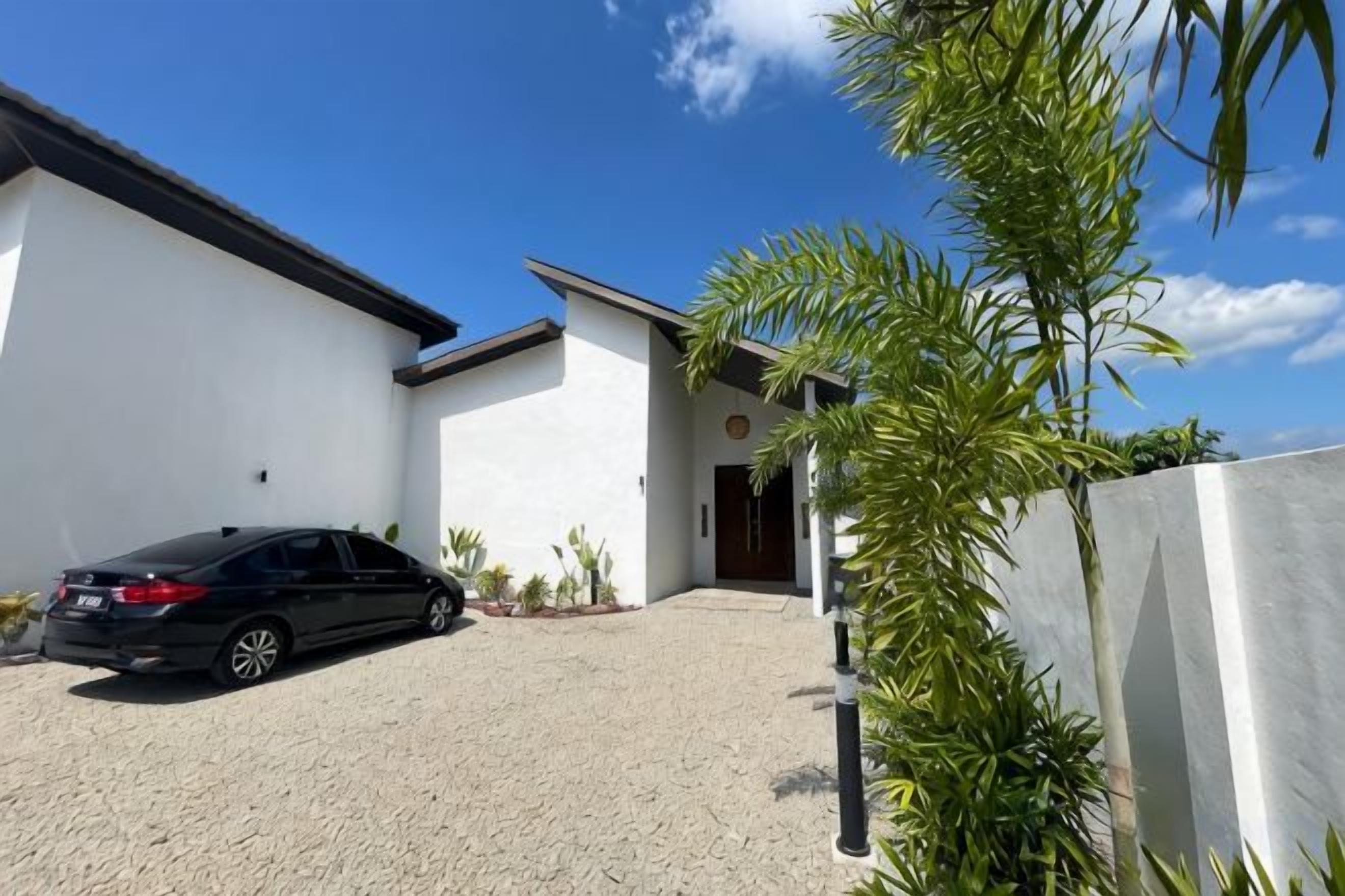 A modern building with a car parked in front, a gravel driveway, and a clear blue sky.