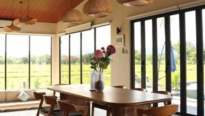A dining area with a wooden table and chairs, large windows, and hanging woven light fixtures. - Villa Moo Moo (Langkawi)