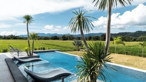 A swimming pool with tiered seating and palm trees, surrounded by a lush landscape and distant mountains. - Villa Moo Moo (Langkawi)