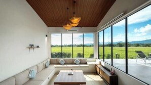 A modern living room with a large window, a sofa, a coffee table, and a hanging light fixture. - Villa Moo Moo (Langkawi)