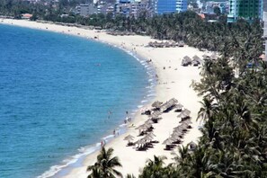 A beach with rows of palm trees and beach umbrellas, a sandy shore, and a clear blue sea. - Cherry Apartment & Hotel (Da Nang)