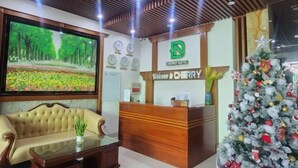 A reception desk with a 'Welcome to Cherry' sign, a Christmas tree, and a large TV screen displaying a garden scene. - Cherry Apartment & Hotel (Da Nang)