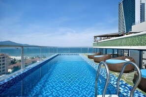 Une piscine à débordement située sur le toit, offrant une vue dégagée sur l’océan, avec une balustrade en verre et un espace salon extérieur.