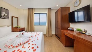 A hotel room with a bed, a desk, a TV, a wardrobe, and a window with a view. - Cherry Apartment & Hotel (Da Nang)