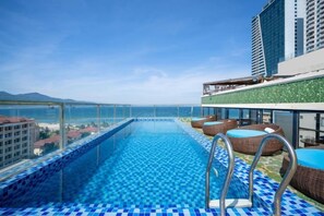 Una piscina infinita al terrat amb vista despejada al mar, gandules i barana de vidre.