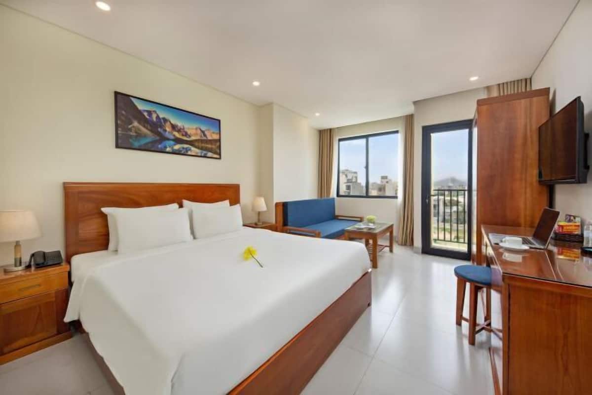 Una camera d'albergo con un letto grande, una scrivania con un portatile, una sedia, un divano, una TV e un quadro appeso al muro.