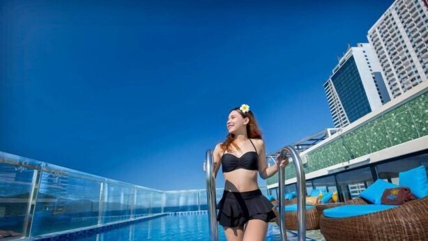 A poolside area with a clear blue sky, a person in a black swimsuit, and a building with balconies in the background. - Cherry Apartment & Hotel (Da Nang)