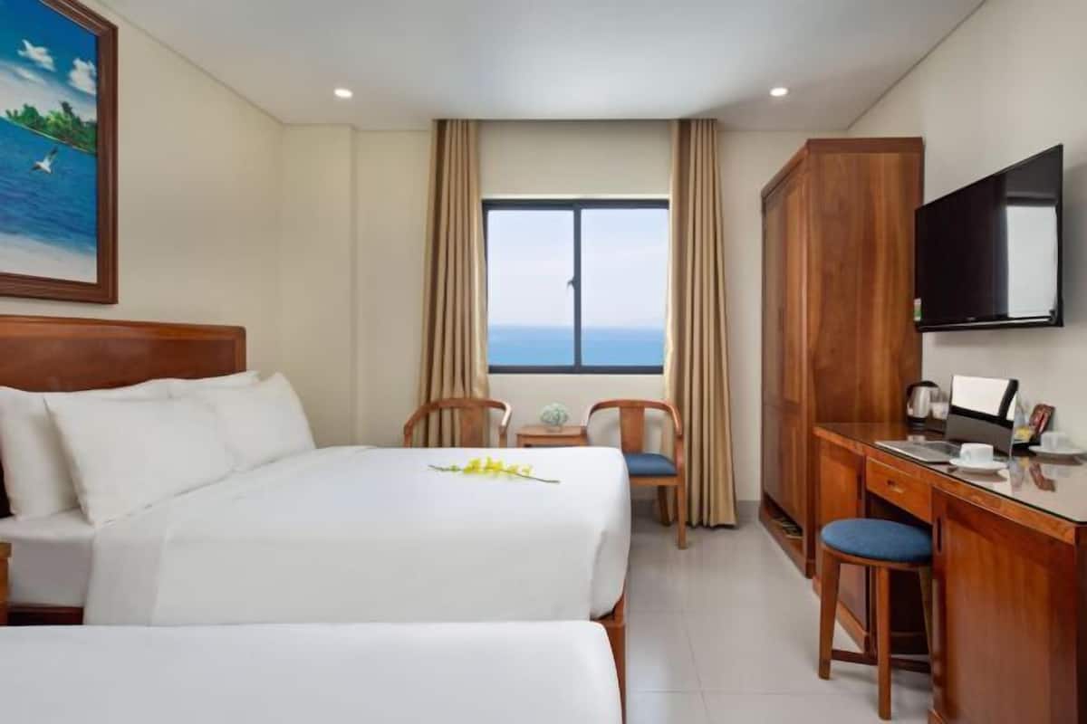 Una camera d'albergo con due letti, una scrivania, una TV e una finestra con vista.