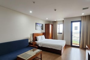 Ein Hotelzimmer mit einem Bett, einem blauen Sofa, einem Nachttisch aus Holz, einem Tisch mit Lampe, einem Gemälde an der Wand und einer Balkontür.