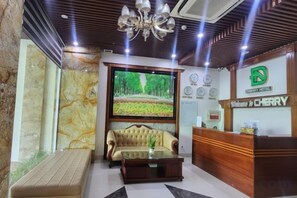 A hotel reception area with a sofa, a coffee table, a TV screen, a reception desk, and a chandelier. - Cherry Apartment & Hotel (Da Nang)
