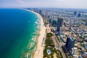 An aerial view of a coastal city with a beach, high-rise buildings, and a dense urban area. - Cherry Apartment & Hotel (Da Nang)