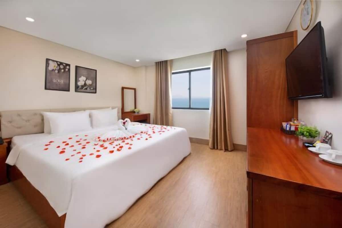Camera d'albergo con un letto, una televisione, una scrivania in legno, una finestra con tende e opere d'arte alle pareti.