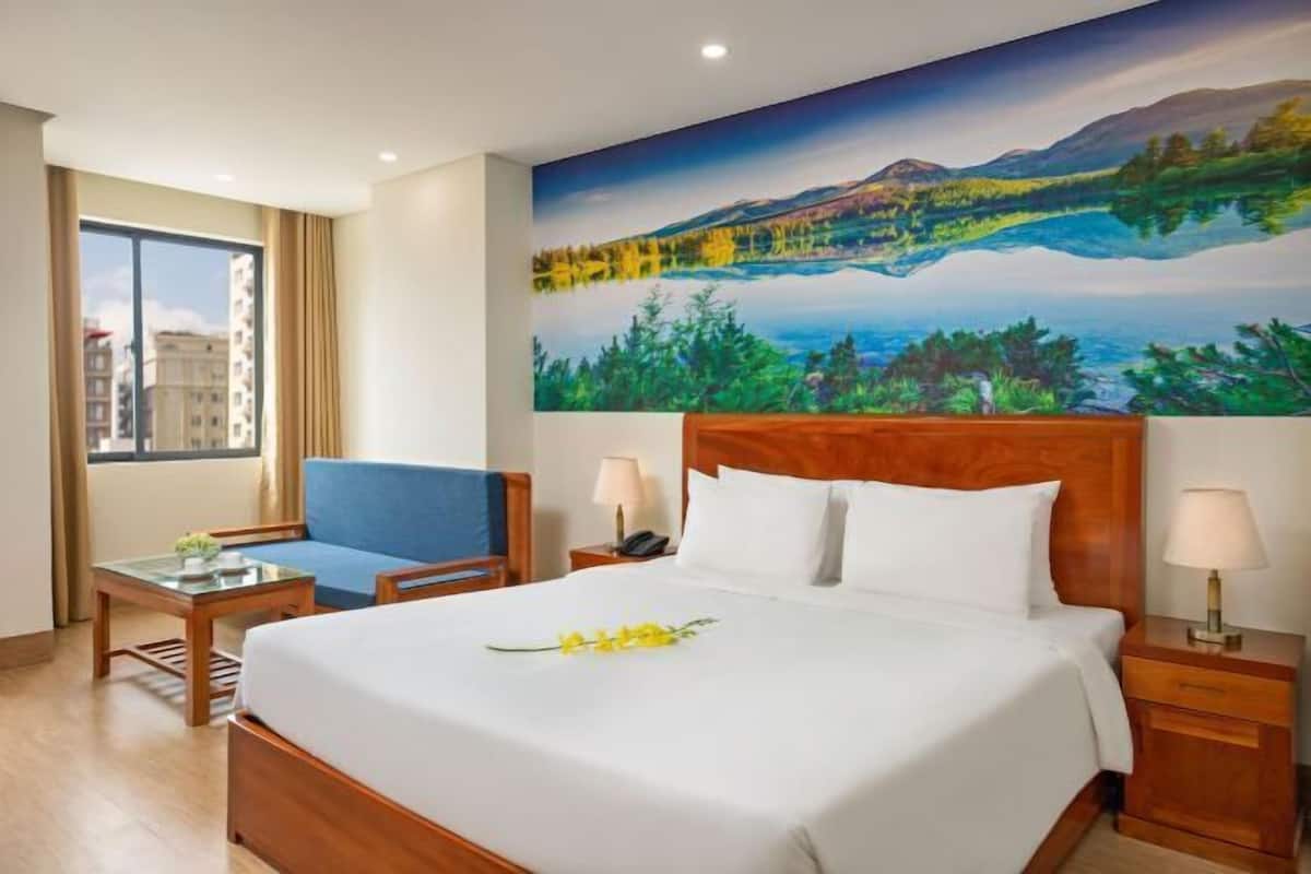 Una camera d'albergo con un letto grande, una scrivania, una sedia, un comodino e un quadro raffigurante un paesaggio.