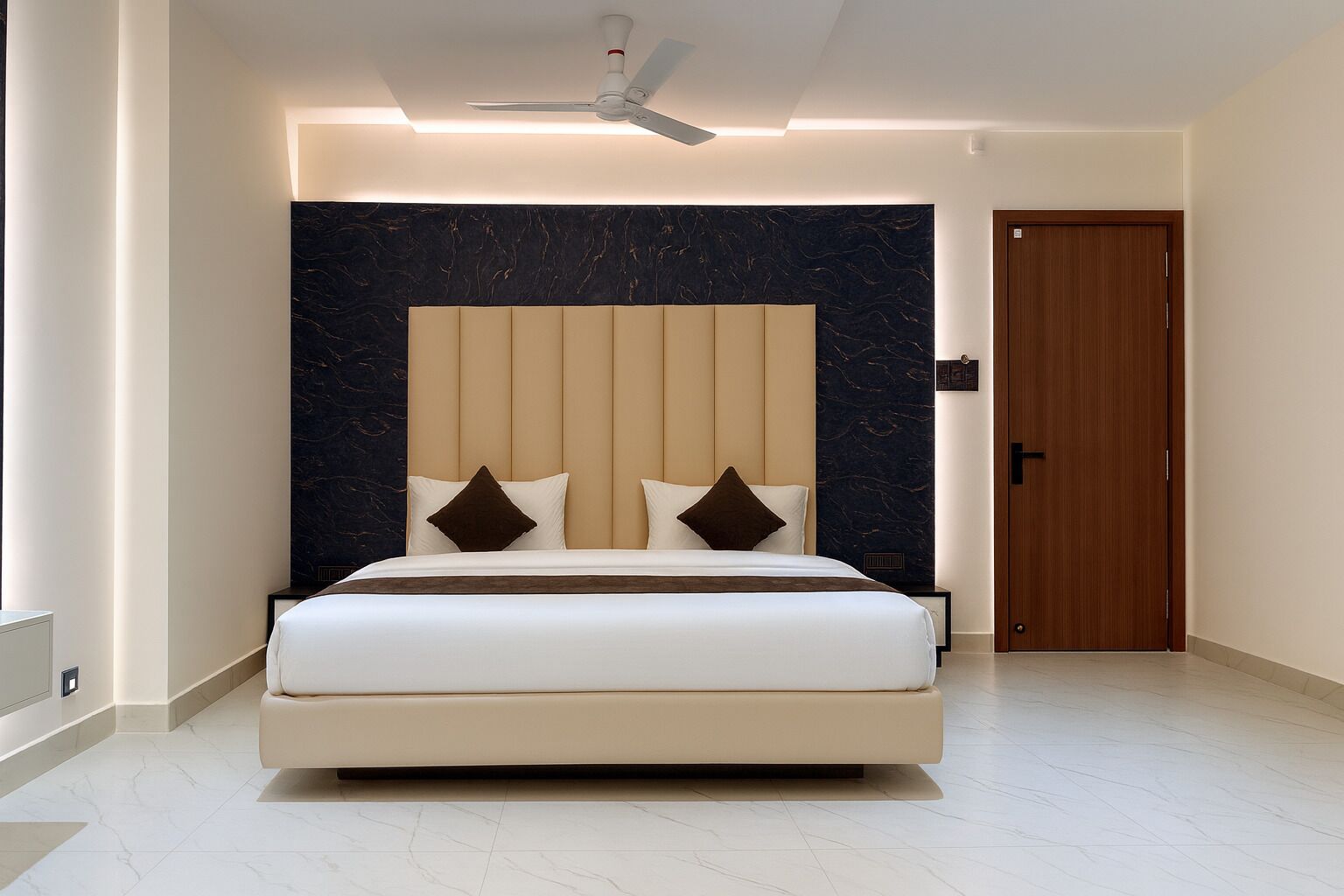 Une chambre moderne avec un grand lit, une tête de lit en marbre et un ventilateur de plafond.