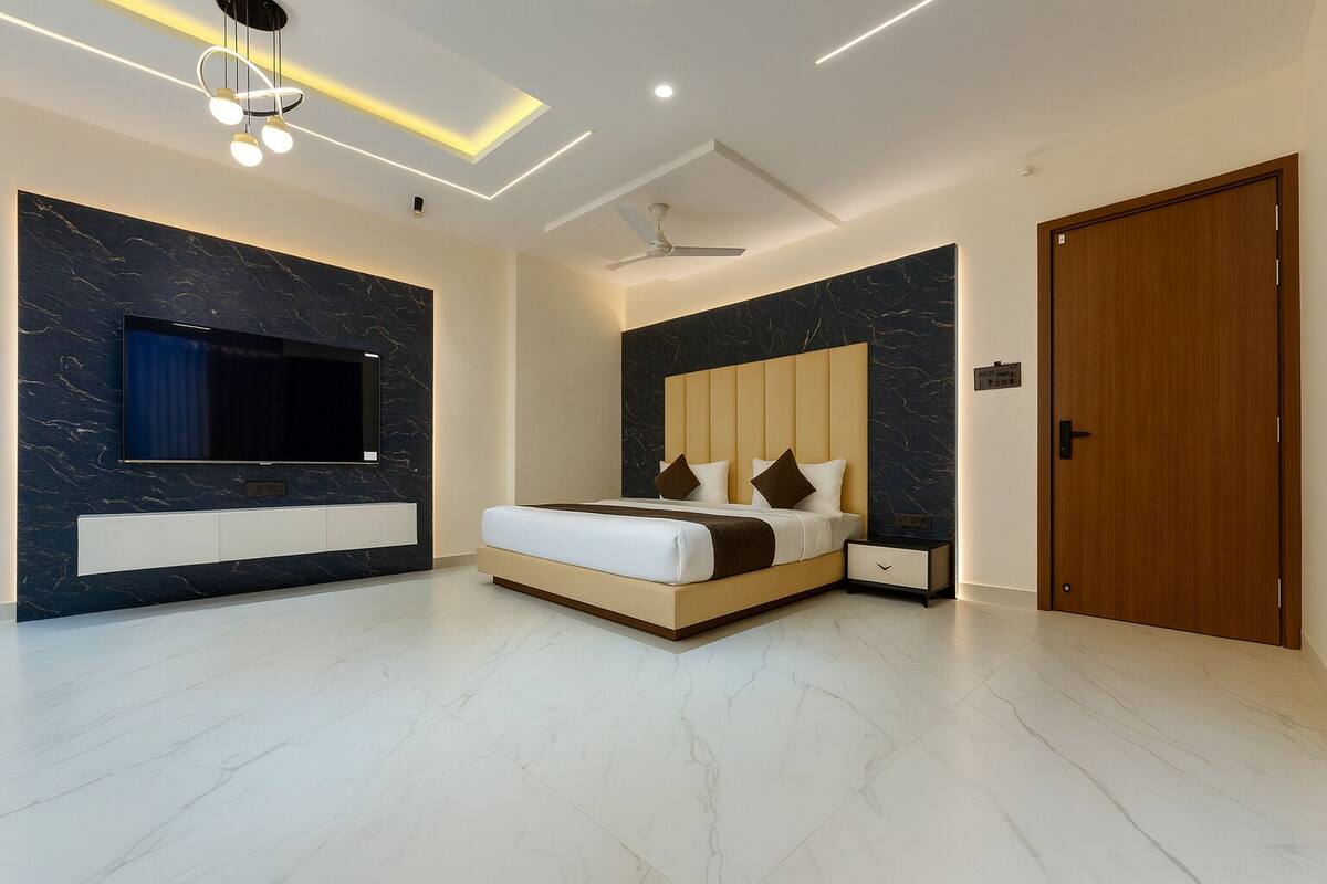 A modern bedroom with a large bed, a TV mounted on the wall, and a wooden door.