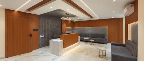 A modern reception area with a marble floor, wooden accents, a reception desk, a sofa, and two small tables.
