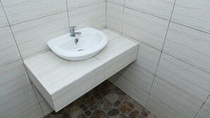 A bathroom with a white sink, tiled walls, and a stone floor. - Citra Homestay Soe (Soe City)