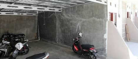 Un área de estacionamiento techada con paredes de hormigón y techo metálico, con varias scooters estacionadas.