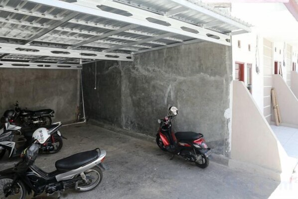 A covered parking area with concrete walls and a metal roof, containing several parked scooters.