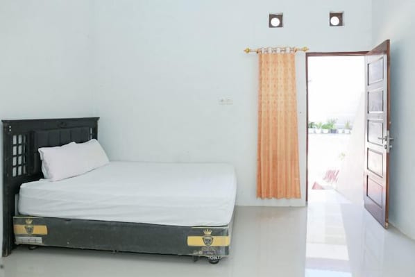 A single bed with a dark headboard and white bedding in a room with a white wall and a door leading outside.