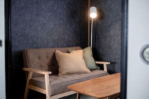 Un sofá con reposabrazos de madera, una mesa y una lámpara en una habitación con pared oscura y texturizada.