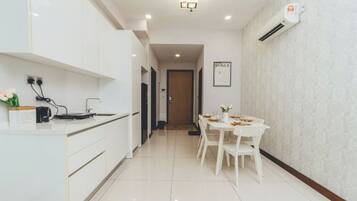 A modern kitchen with white cabinetry, a dining area with a white table and chairs, and an air conditioning unit on the wall.